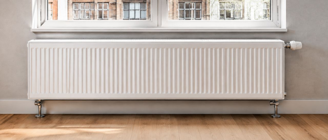 Illustration photoréaliste : radiateur blanc à panneaux avec robinet thermostatique, sous une fenêtre