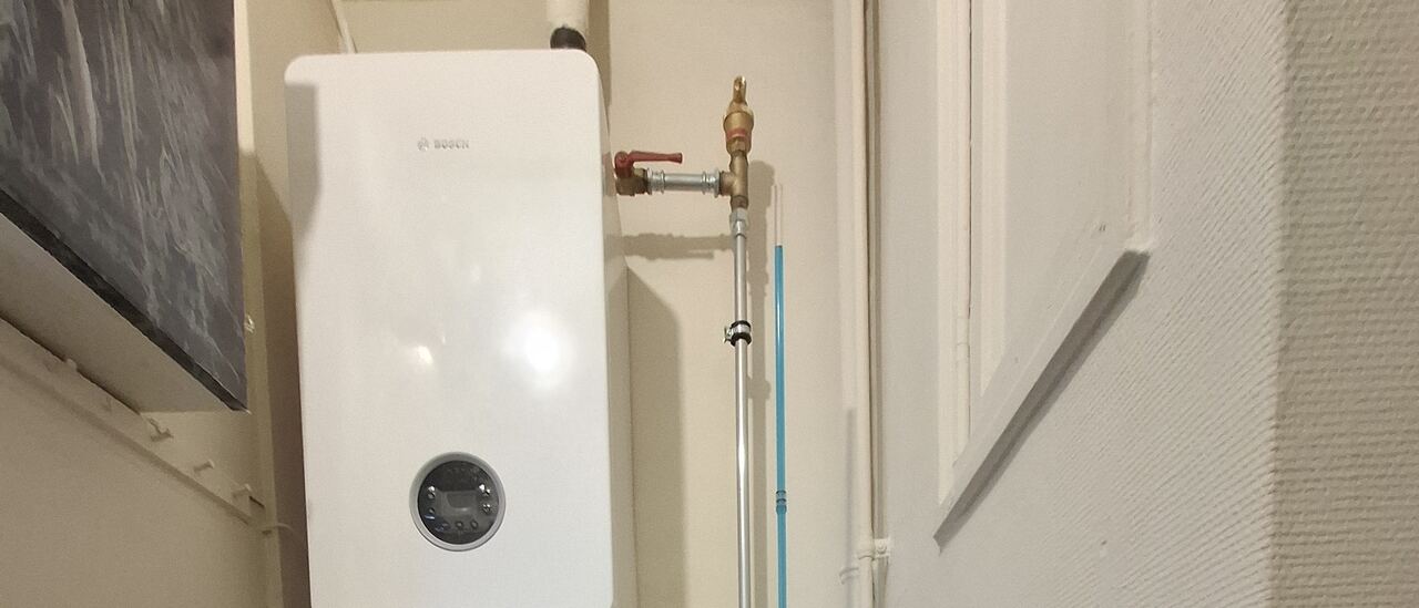 Chaudière murale gaz à condensation Bosch installée par Atmos Technics dans un couloir technique à Bruxelles, vanne d'arrêt gaz et raccordements cuivre apparents.