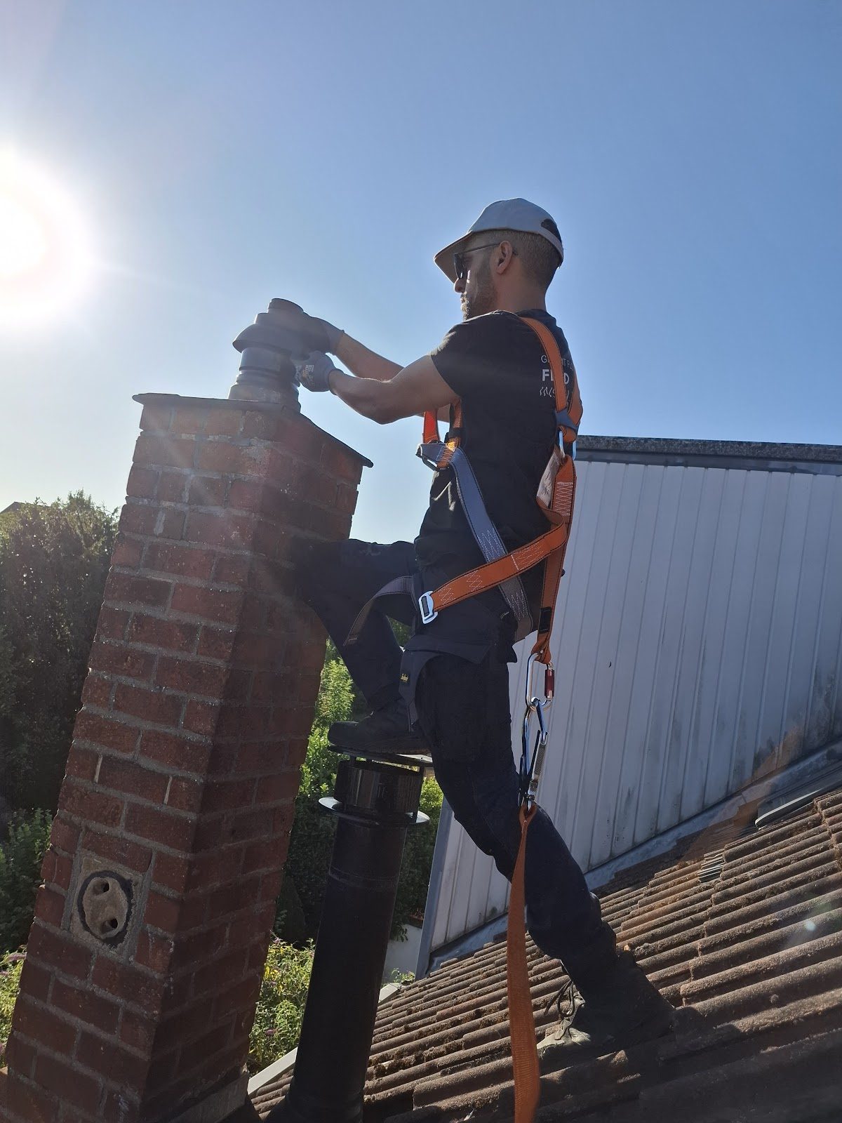 Technicien équipé d’un harnais, d’une casquette et de gants, intervenant sur une sortie de cheminée en toiture.